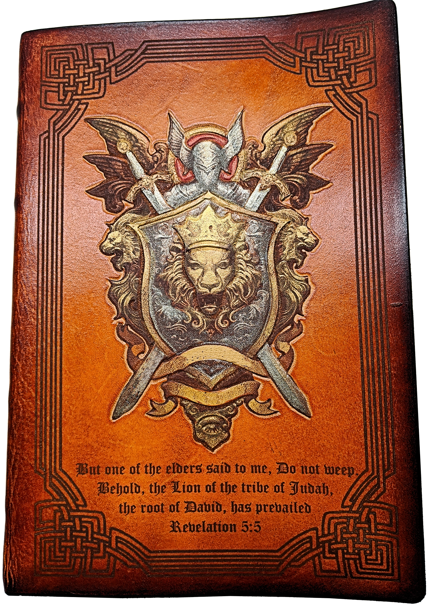 A custom leather bound bible with a coat of arms and Celtic border, custom engraved and hand painted with metallic highlights. Text reads: But one of the elders said to me, Do not weep. Behold, the Lion of the tribe at Judah, the root of David, has prevailed. - Revelation 5:5